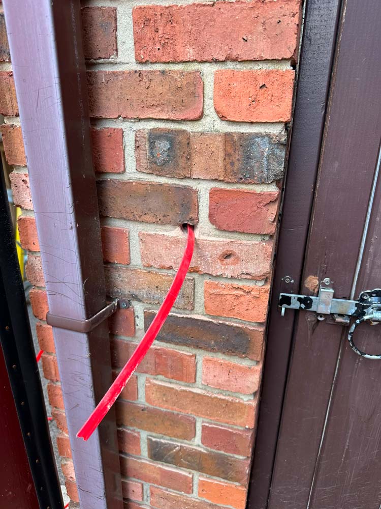 EV charger cable route prepared through exterior brick wall
